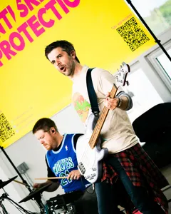 The bassist mid-shout under the yellow banner, drummer behind him