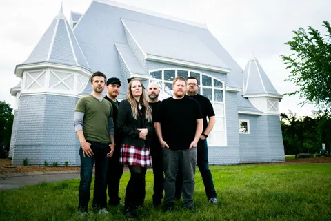 The whole band posed on the lawn in front of a lakeside pavilion
